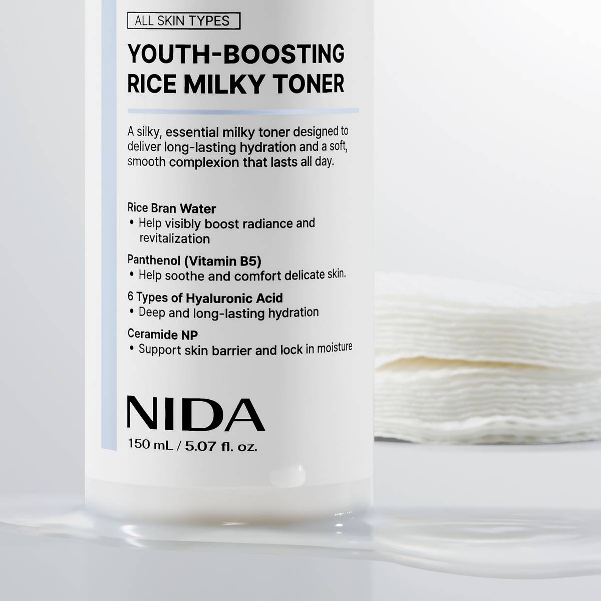 Close-up of the NIDA Youth-Boosting Rice Milky Toner 150 ml bottle beside stacked cotton pads