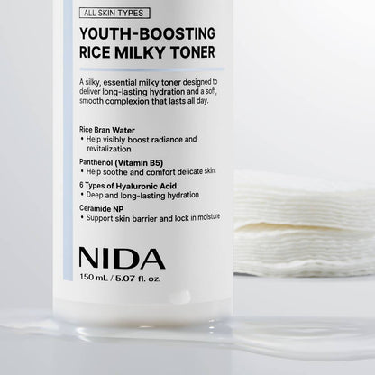 Close-up of the NIDA Youth-Boosting Rice Milky Toner 150 ml bottle beside stacked cotton pads
